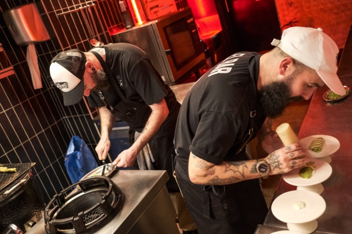 El chef emplata el repollo brasa mientras su ayudante trabaja detrás.