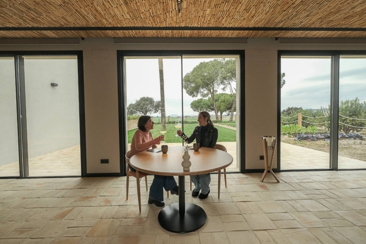 Dos mujeres brindan en la sala del restaurante cuyos ventanales dan al jardín.