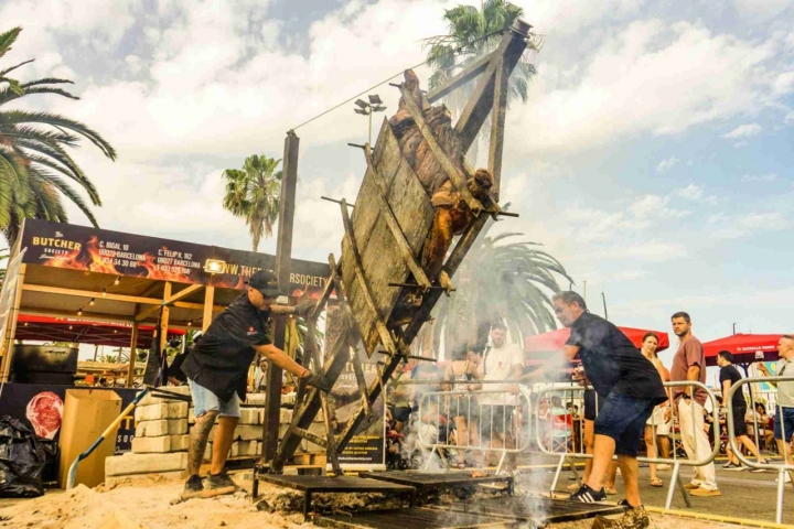 Maestros parrilleros girando una enorme parrilla con carne.