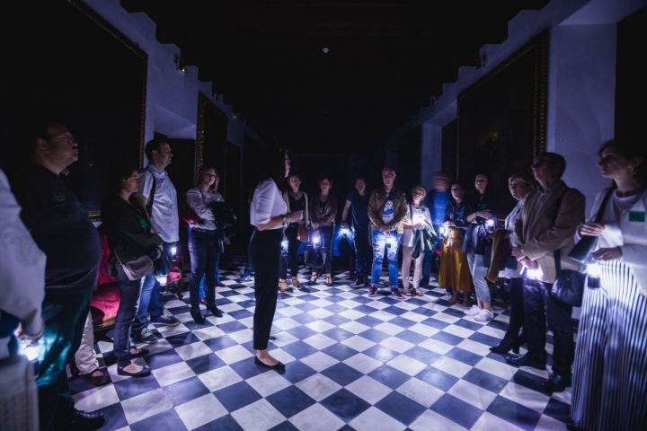 La guía de Engranajes Culturales recibe a los visitantes a la entrada del Hospital de la Caridad durante la visita nocturna, en Sevilla.